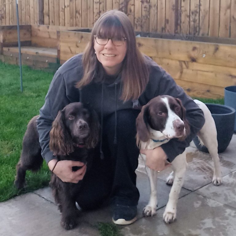Woman kneeling on grass, holding two dogs, a brown cocker spaniel and a springer spaniel.